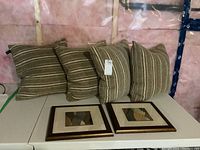 Four down filled throw cushions with striped pattern and two framed prints below cushions.
