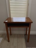 Photo of a solid wood desk with one shelf, showing front and top views. Desk has visible wear and scratches on the surface.