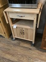 Front view of the light wood kitchen cart with drawer and cabinet doors, microwave on top.