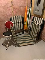 Photo showing 2 foldable lawn chairs with white/green stripes, a foldable lounge chair with green/beige stripes, 2 foldable stools with black/red seats, and 2 beach umbrellas in the corner.