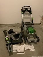 Overview of mower, blower, charger, battery and manuals on concrete floor