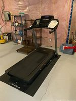 Full view of NordicTrack treadmill on black mat in basement corner showing treadmill surface, frame and surroundings.