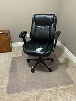 View of black vinyl swivel office chair on transparent hard plastic floor protector mat against beige carpet and wall