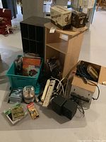 Wide view showing laminate media shelf, power bars, cords, office supplies in plastic bin and boxes.