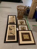 Overview of all five framed prints arranged on floor with rattan basket beside them.