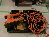 Photo showing the full tool inside its black carrying case along with a long orange power cord coiled beside it