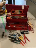 Full view of open red metal toolbox with hand tools and extension cords around it.