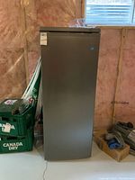 Front view of grey Danby upright freezer standing in unfinished basement.