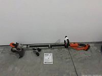 Full view of the Black + Decker cordless trimmer edger laid on floor with charger and instruction manual nearby.