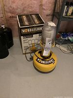 Wobble Light work light shown standing next to its original box on a basement floor near shelving.