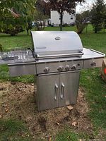 Front view of Glen Canyon stainless steel BBQ grill showing lid, control knobs, side burner, and storage cabinet with double doors below.