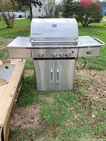 Front view showing four control knobs, side shelves, and storage cabinet doors below, with grill hood and temperature gauge visible.