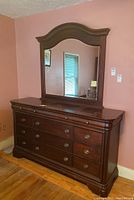 Front angle of dark wood dresser with 12 drawers and attached mirror showing details of drawer handles and curved top frame
