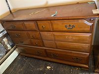 Front view of the wooden dresser with six drawers, showing some missing handles and surface wear.