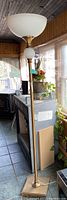 Full vertical view of the gold floor lamp showing the white globe glass shade and decorative spherical accent on the stem, standing next to a fireplace and window in a room.