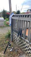 Multiple fishing rods with spinning reels and leather grips leaning against wood fence outdoors.