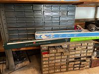 Metal storage cabinets with many small drawers filled with assorted hardware parts such as screws, nuts, bolts, nails, washers, and cotter pins. Some drawers are open showing contents.