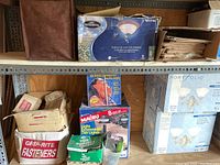 Metal shelving with boxes of outdoor light fixtures, magazines, and hardware supplies.