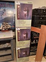 Stack of three boxes for Portfolio outdoor wall lanterns with rust finish and clear glass shade visible in product image on boxes.