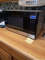 Panasonic NN-SN67HS microwave oven on kitchen counter, side angle showing digital display lit up and control panel.