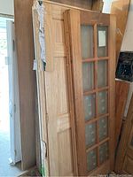 Stack of wooden doors, some with glass panels and some solid, visible scratches and packaging tape on some doors