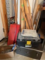 Photo showing scrap wood planks, tool boxes stacked, metal chains hanging, and box with metal hinges.
