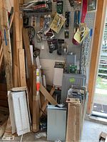Photo showing scrap wood, window shutters, circuit breaker boxes and assorted items stacked in a garage space near the door.