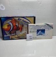 Photo showing the original boxed remote control flying clownfish toy and the Whitewing paper airplanes kit together.