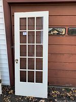 Full white French door with 15 glass panes in a 3x5 grid shown standing upright outside.