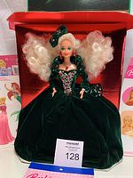 Holiday Barbie doll seated in red-lined box wearing green velvet gown with curly blonde hair and red-green sequin bodice detail.