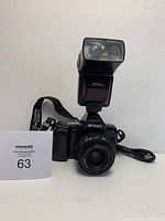 Front view of Nikon F-801 camera with attached Speedlight SB-24 flash, showing lens and camera body with strap and cord.