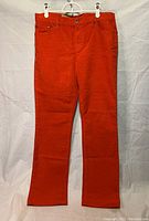 Front view of the red-orange corduroy pants hanging on a white hanger, showing full length and button closure.