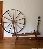 Side view of antique wooden spinning wheel showing large circular wheel, spindle, base, and four legs