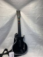 Full body shot of the black Gibson-branded Xbox Guitar Hero guitar controller showing the entire front with colored fret buttons, whammy bar, strum bar, and strap.