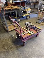 Red rolling cart with flat platform and adjustable lever control, holding various tools and tennis rackets (not included in sale). The cart is visibly worn with paint chipping.