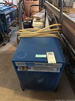 Blue Dry Pro 5000 industrial desiccant air dryer with power cord coiled on top, placed in a workshop environment.