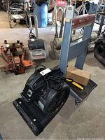 Photo showing black Air Foxx fan with power cord resting on blue rolling cart with caster wheels.