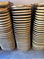 Stacks of many beige folding chairs showing the side of the metal frames with wear on paint and scuff marks