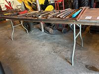 Long side view of a folding table illustrating metal legs and wooden top loaded with assorted metal tools.