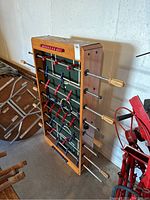 Foosball table leaning against a wall showing handles and player rods.