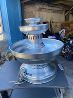 Single silver metal tiered fountain with a broad basin and a smaller top bowl, electric cord visible at base.