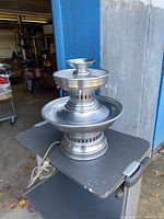 Full view of electric metal water fountain with silver finish on a table outdoors.