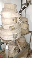 Stacked fire hoses coiled and placed on metal shelving with visible metal coupling connectors and labeling on hoses.