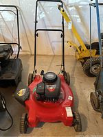 Front view of red Briggs and Stratton lawn mower with black handlebar and engine cover showing brand and engine details.