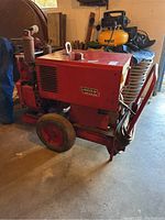 Red Lincoln arc welder unit with wheels and cables visible in well-lit garage setting.