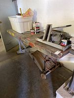 Full side view of the motorcycle jack with various tools and items on top including a white plastic bin, metal lever, paint cans, and ramp attachment.