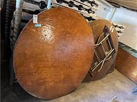 Three round wood veneer table tops leaning against stacked white plastic folding tables