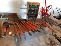 Overview of all assorted long-handled tools laid on a wooden table including pipe wrenches, chisels, hooks and bolt cutters