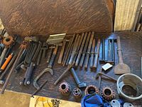 Overview of assorted hand tools on wooden table, showing chisels, pipe wrenches, clamps, dies and hammers