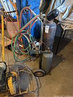 Oxygen and acetylene tanks on a metal cart with hoses, regulator, and torch. Tanks are chained to the cart.